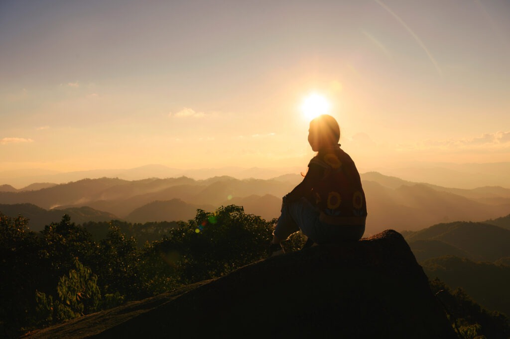 Successful silhouette young hiker woman relaxing and enjoying the sunset view on top of mountain peak at national park