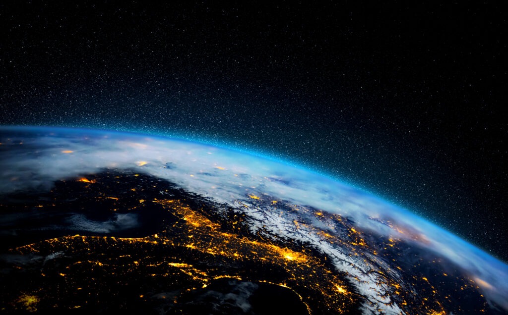 View of Earth from space at night, showing international city lights glowing across the curved horizon against a starry sky.