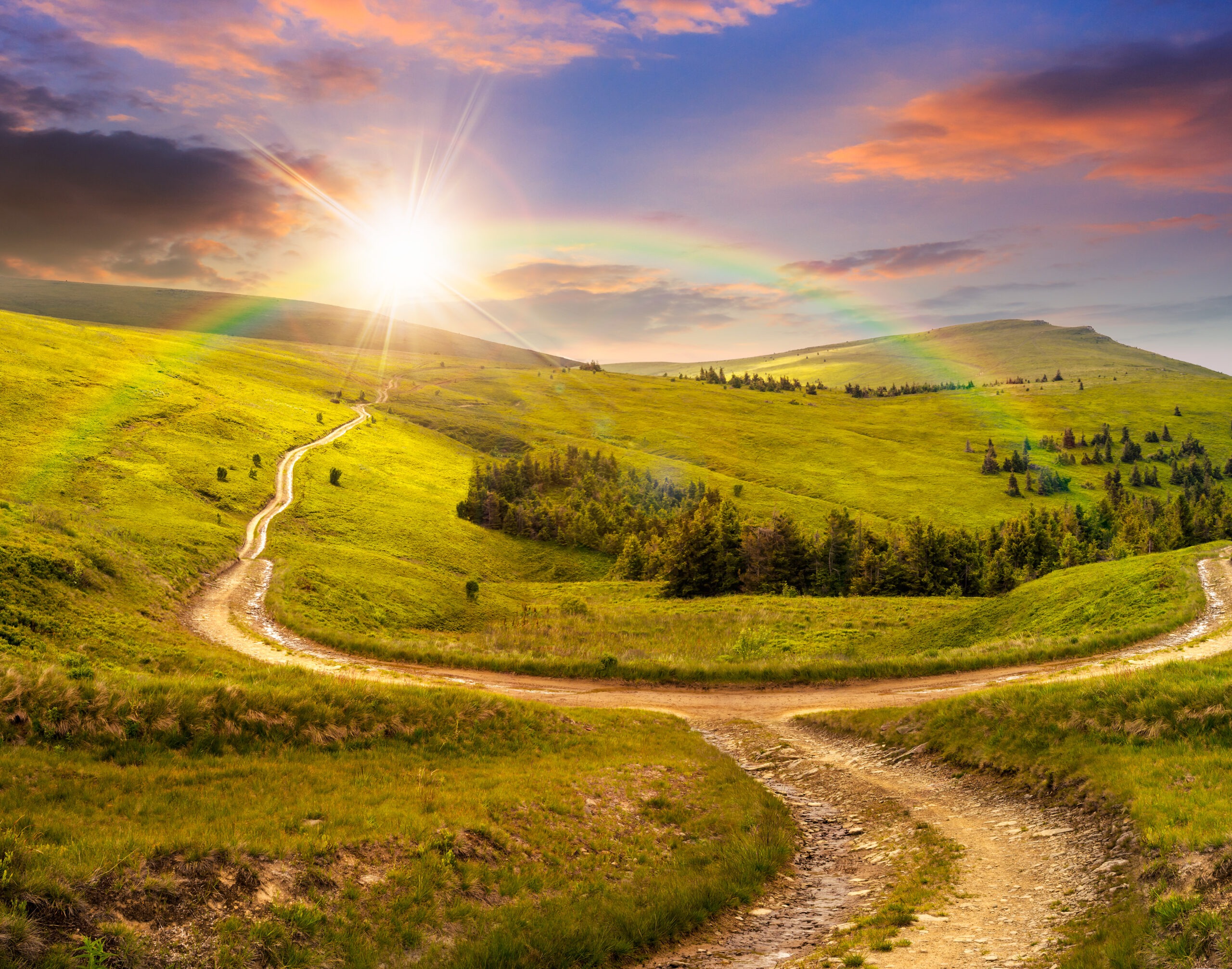 Two dirt paths merge into one winding trail across green hills, with a rainbow arcing beneath a rising sun.